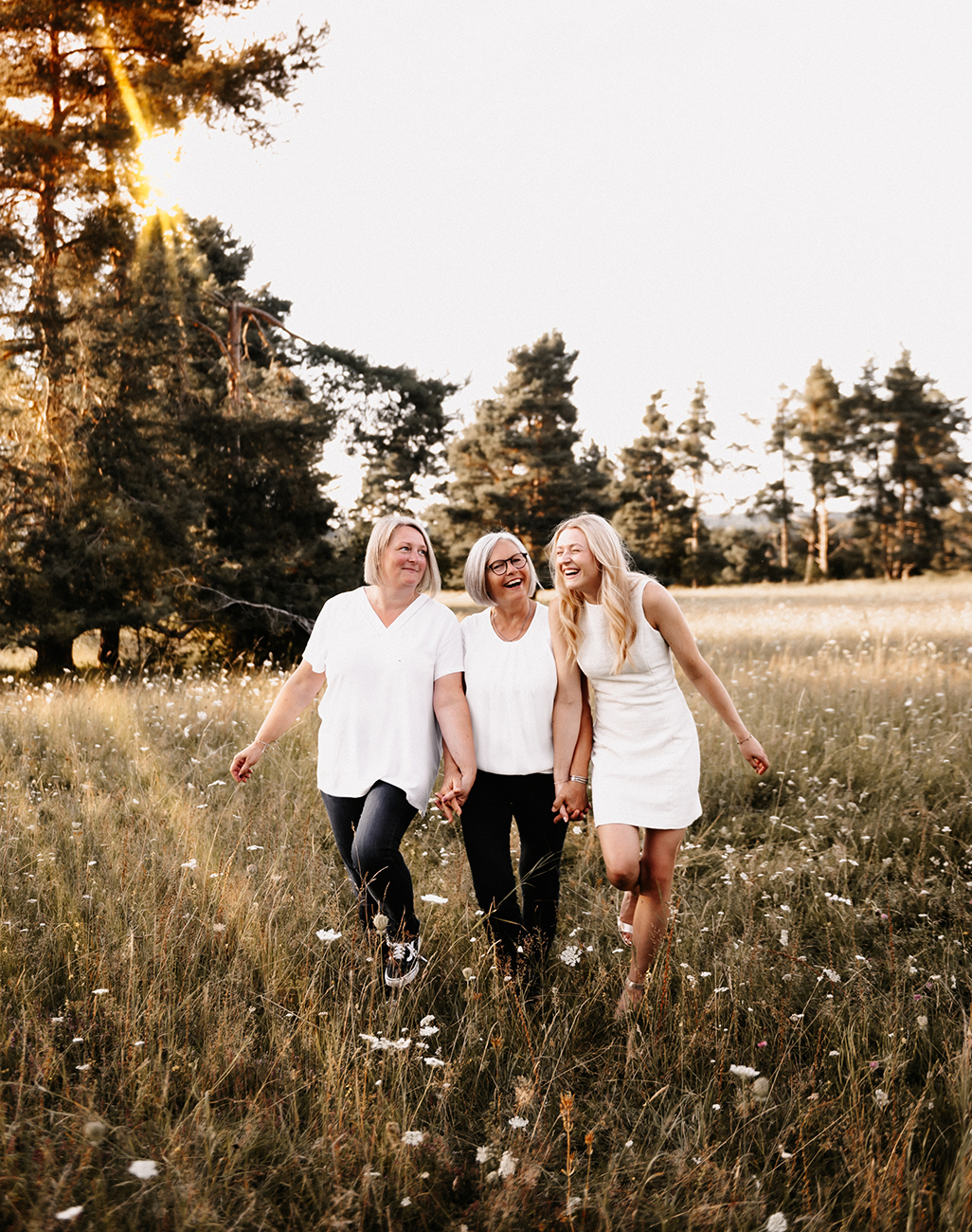 Drei Frauen lachen gemeinsam in einer Wiese im Sonnenuntergang – natürliche Familienfotografie Nürnberg Schwabach Roth Fürth