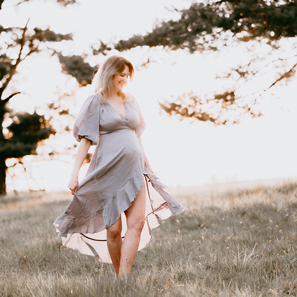 Schwangere Frau läuft barfuß im Gras im Sonnenuntergang – natürliches Babybauch Shooting von Stefanie Cypris Fotografin Nürnberg Schwabach Roth Fürth