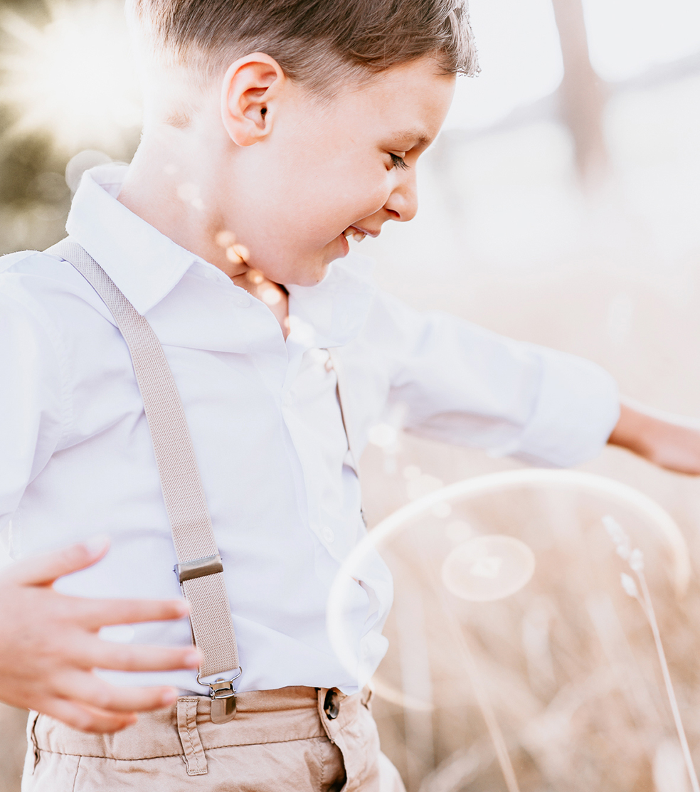 Junge im Hemd mit Hosenträgern spielt im Sonnenlicht im Freien – natürliche Kinderfotografie von Stefanie Cypris Fotografin Nürnberg Schwabach Roth Fürth