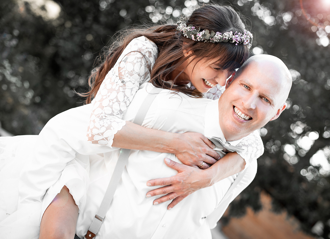 Braut sitzt lachend auf dem Rücken des Bräutigams im Freien – natürliche Hochzeitsfotografie von Stefanie Cypris Fotografin Nürnberg Schwabach Roth Fürth